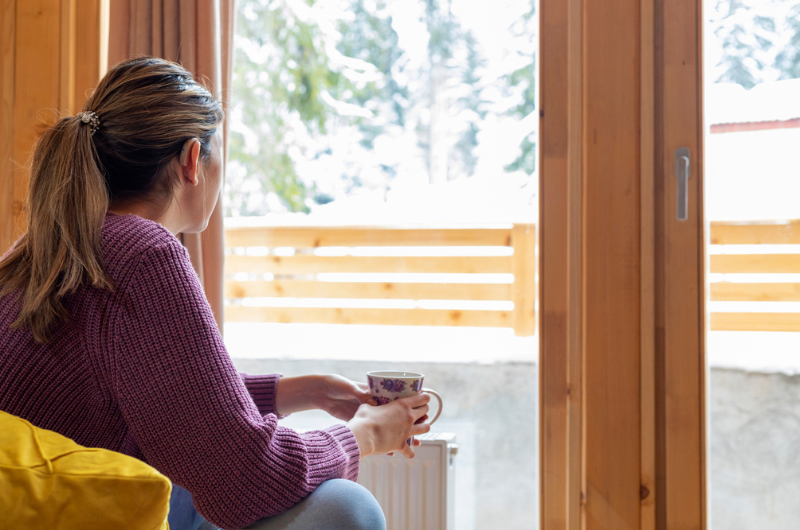  Beautiful young woman with hearing aid drinking tea and enjoying a winter view.