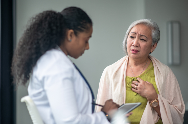 A senior woman shares her chest pain symptoms with her doctor at an appointment.