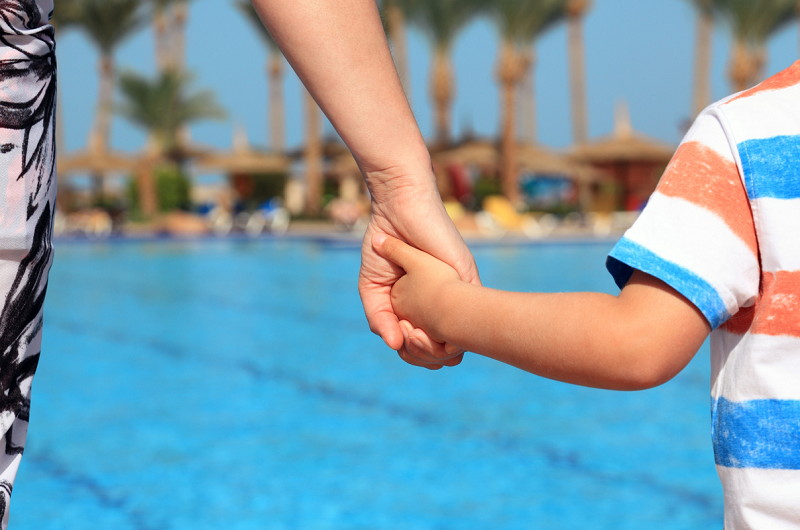 Mother and son holding hands, looking out at a pool.