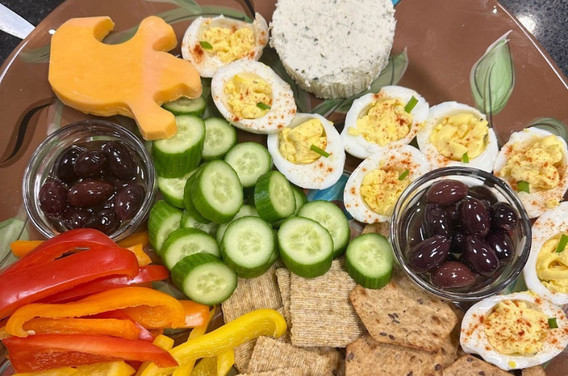 A serving tray full of various crackers, vegetables and deviled eggs.