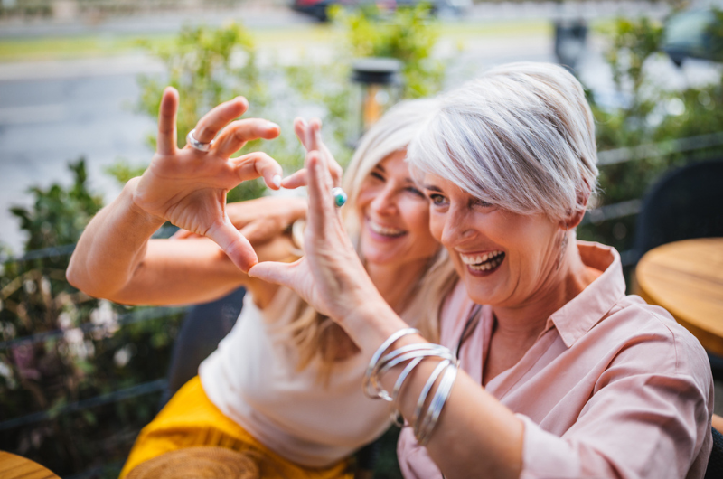 Fashionable senior friends having fun at a restaurant and making a heart symbol with their hands.