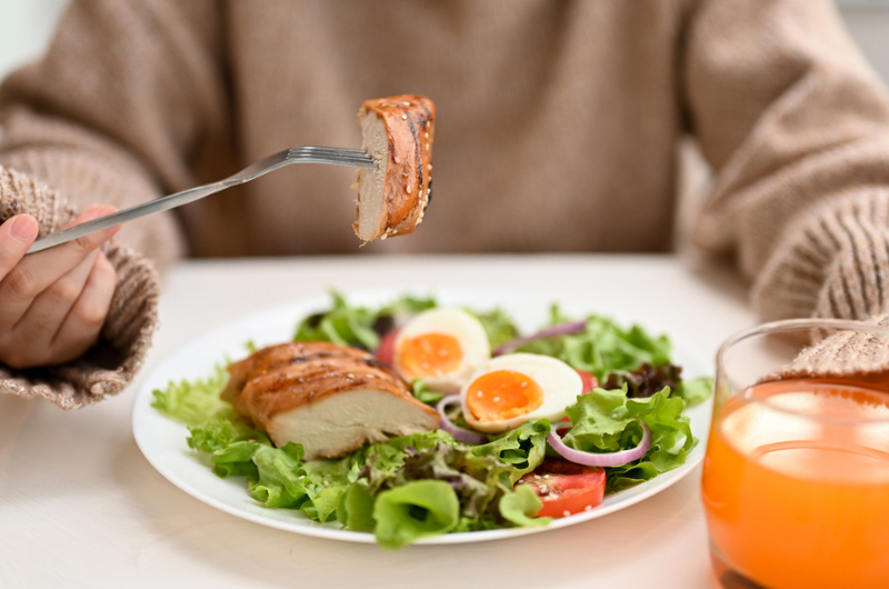 Woman eating a fresh healthy salad with grilled chicken breast.
