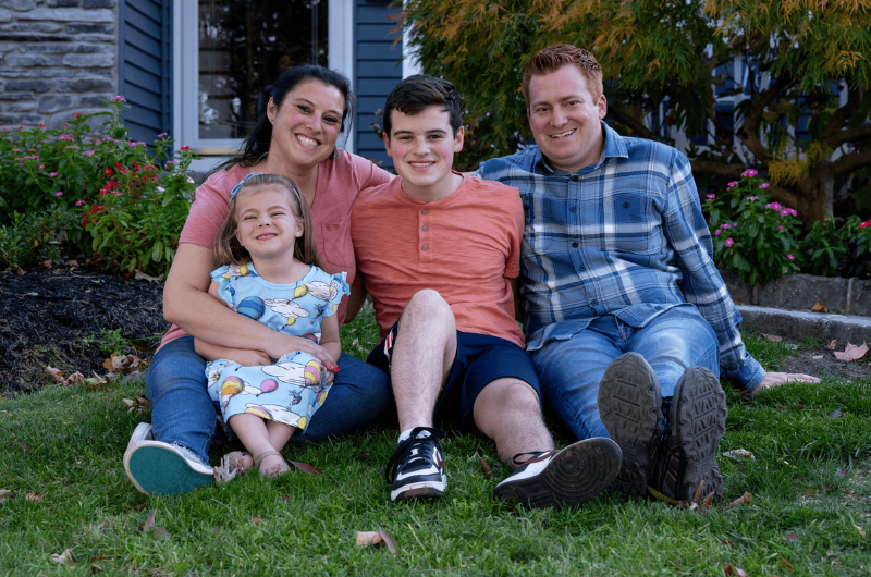 44-year-old Jamie McBride sits on the grass with her husband, son and daughter.