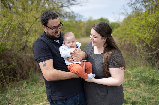 Baby Benny being held by his parents, all smiling, sitting on the couch.