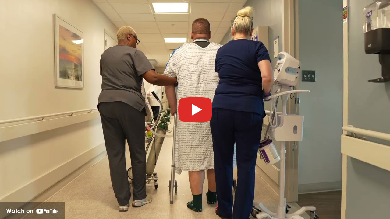 nurses helping a man walk down a hospital hallway