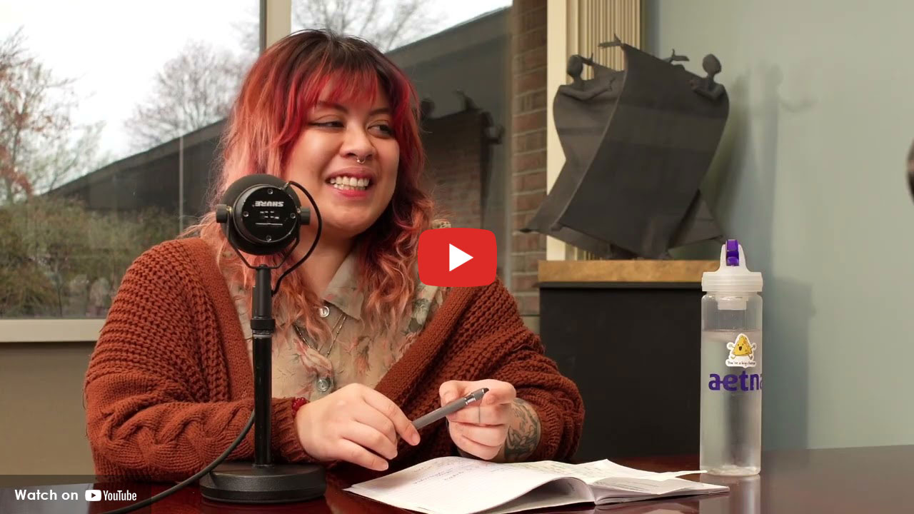 Teen smiling while speaking into a microphone at a table with notes and a water bottle